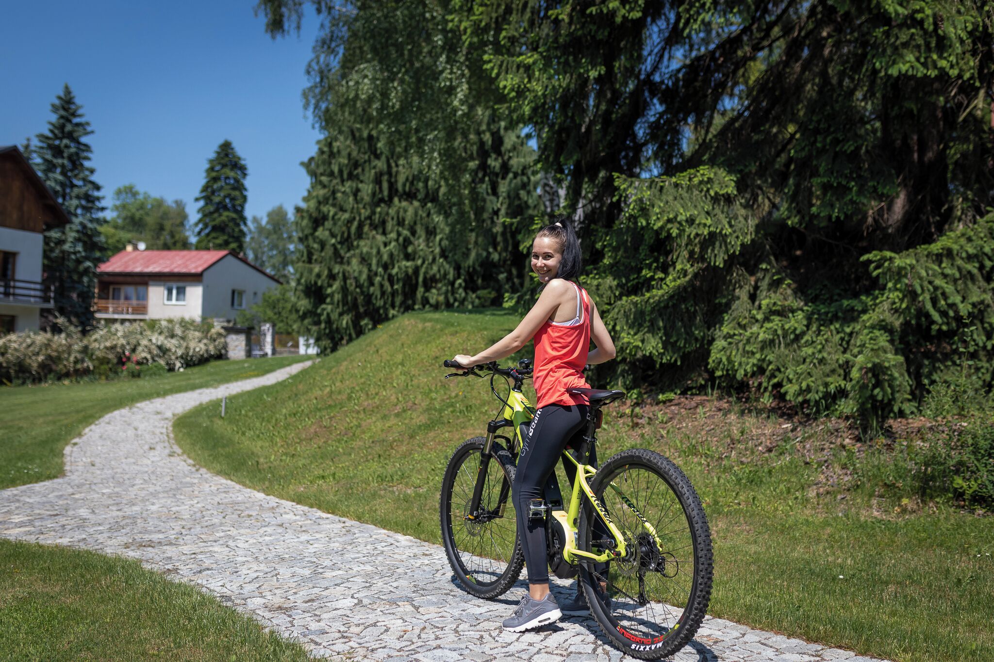 Una persona en bicicleta sobre un camino adoquinado en una zona verde y boscosa, con casas al fondo.