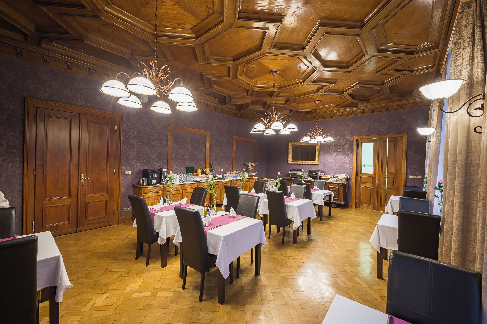 A dining area with wooden ceiling, tables set with white tablecloths, and chairs.