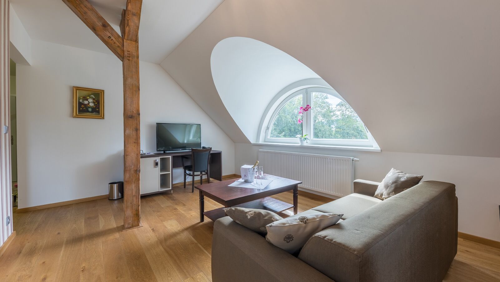 A loft-style room with a wooden ceiling, a large window, a sofa, a TV, and a dining table.