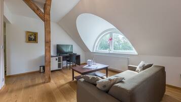 A loft-style room with a wooden ceiling, a large window, a sofa, a TV, and a dining table.