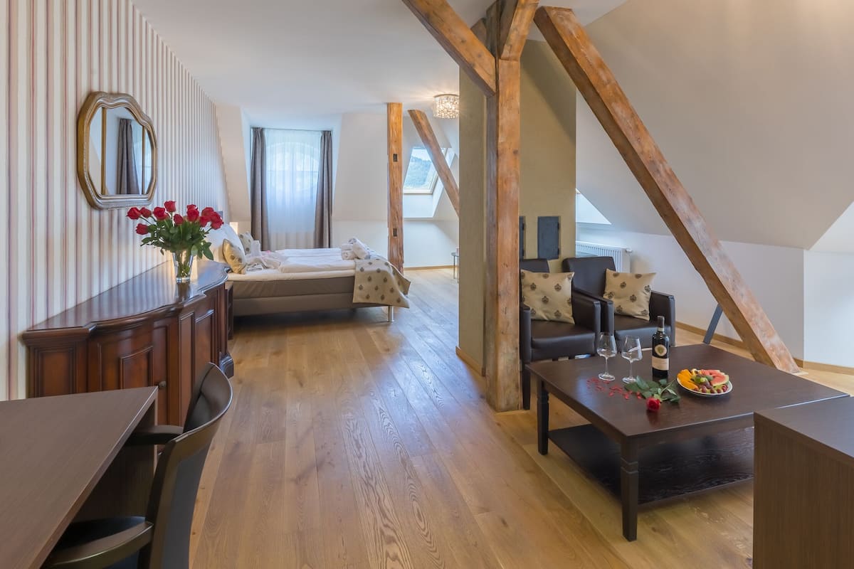Ein gemütliches Zimmer mit einem Bett, einem Esstisch mit Flasche und Gläsern, einem hölzernen Schreibtisch und einem Spiegel an der Wand.