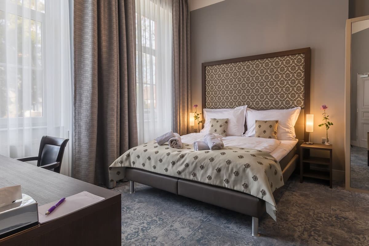 Ein Hotelzimmer mit Bett, Schreibtisch, Stuhl, Nachttisch und Spiegel.