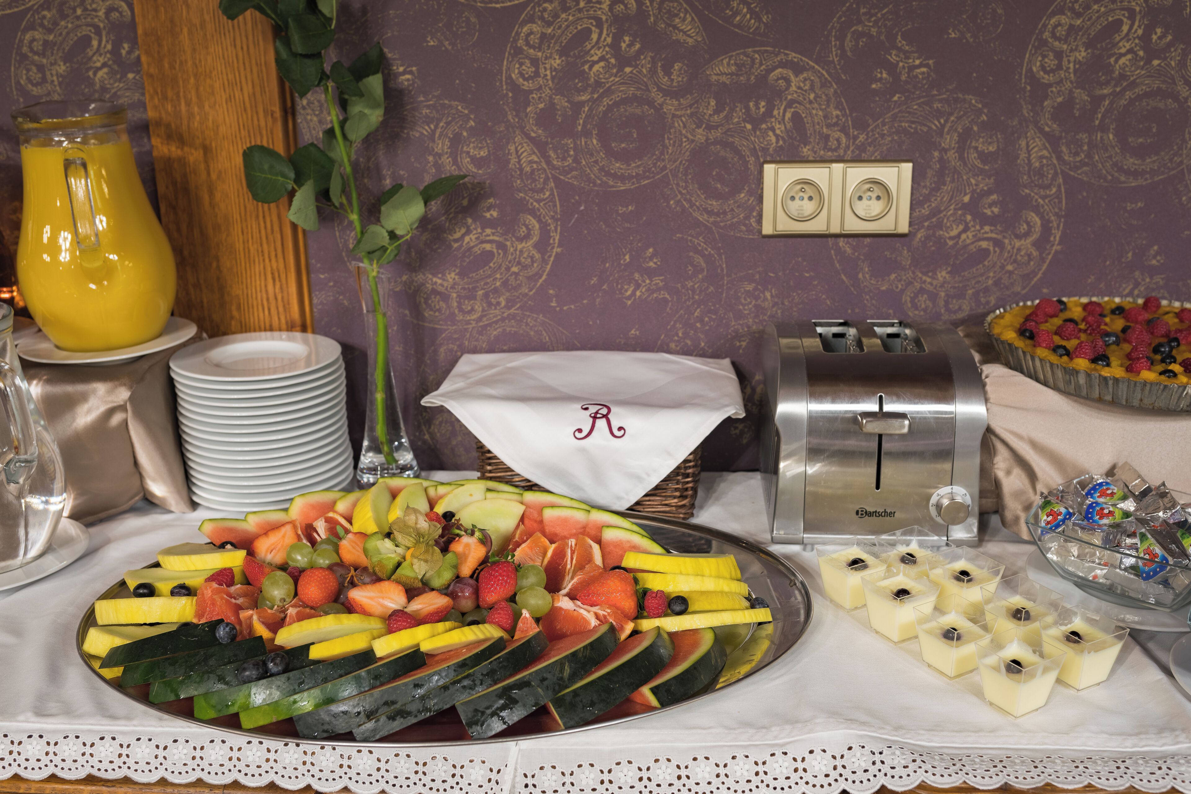 A breakfast buffet with a variety of fruits, a juice pitcher, and a toaster.