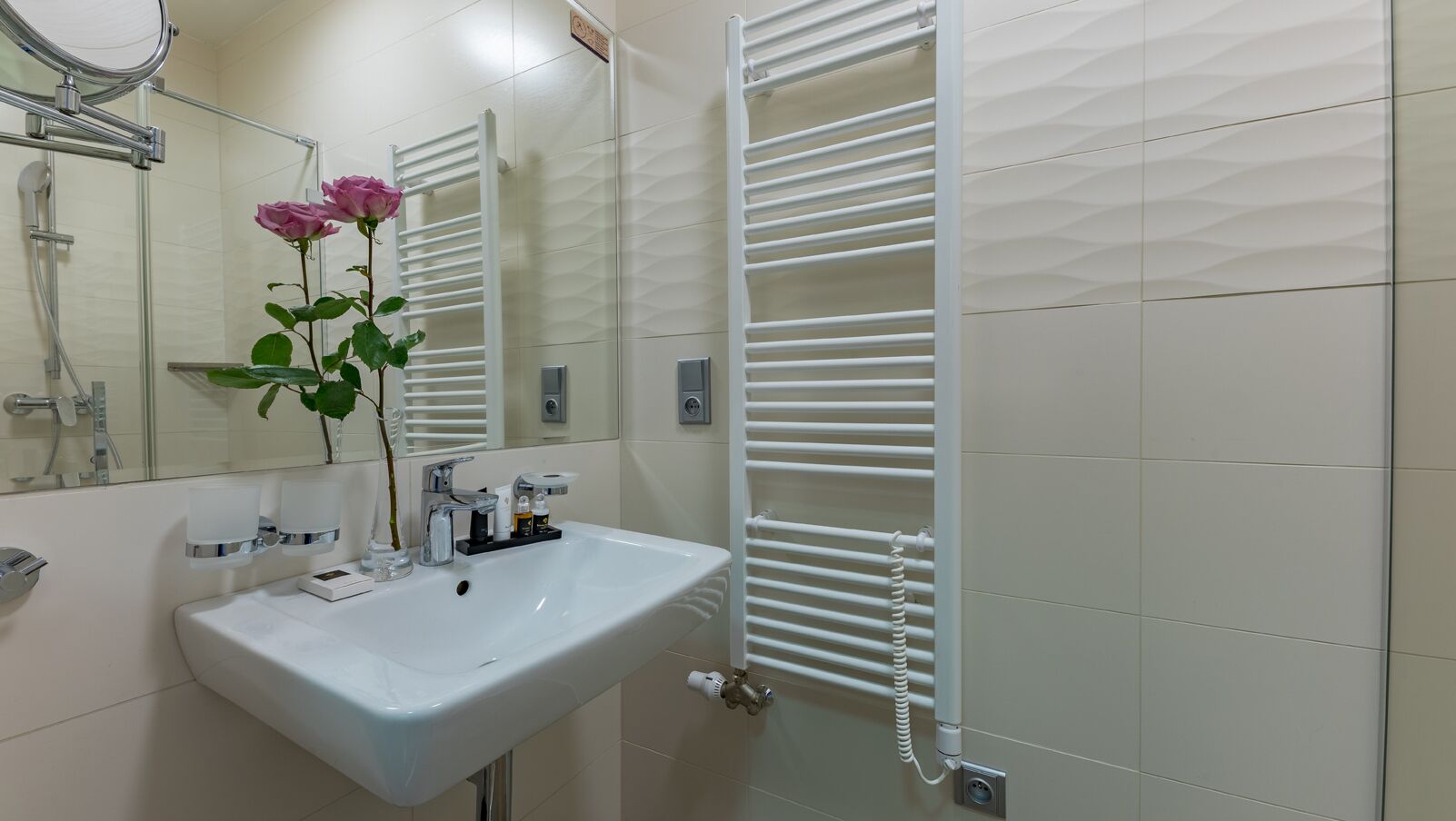 Een badkamer met een wit wastafel, een spiegel, een handdoekhouder en een douche.