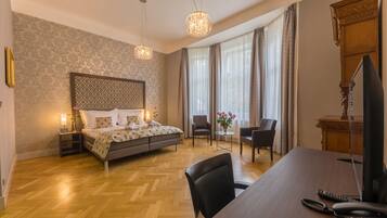 Habitación de hotel con cama, escritorio, silla, televisión y ventana con cortinas.