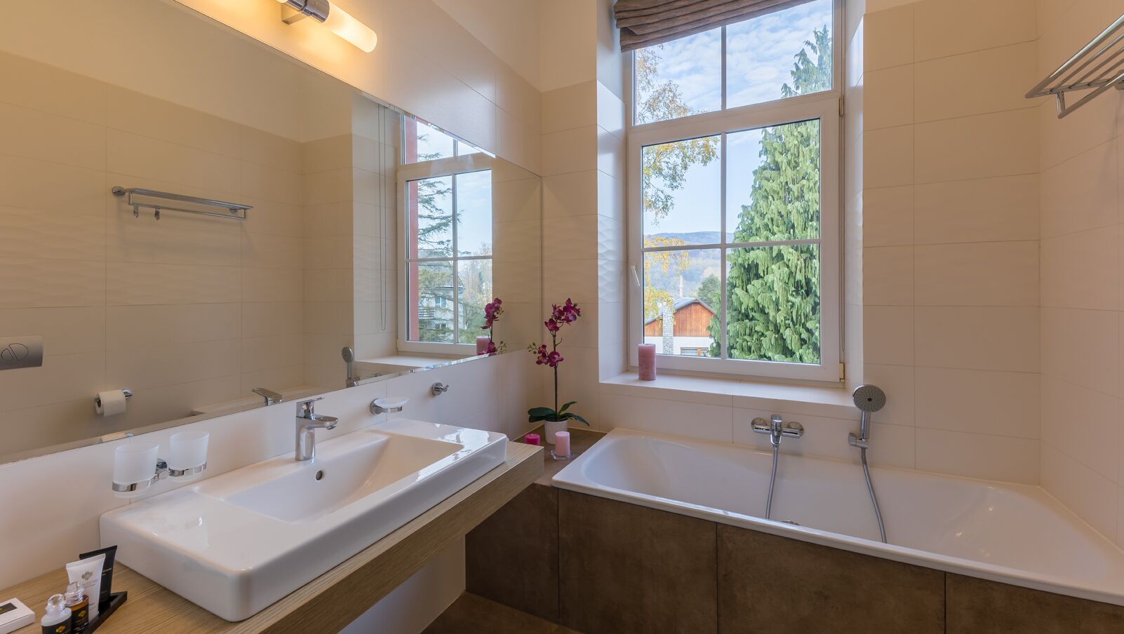 A modern bathroom with two sinks, a large mirror, and a window providing a view of trees and a house.