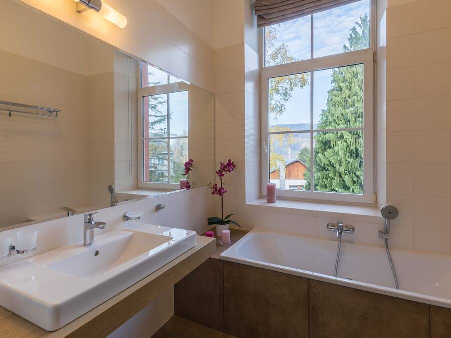 Ein modernes Badezimmer mit zwei Waschbecken, einem großen Spiegel und einem Fenster mit Blick auf Bäume und ein Haus.