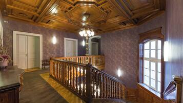 A grand staircase with a wooden railing, a chandelier, and a large window with multiple panes.