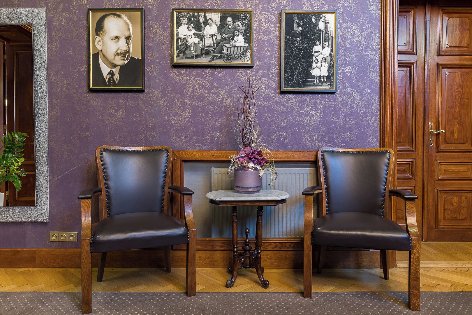 A room with two leather chairs, a small table with a vase, and three framed photographs on the wall.