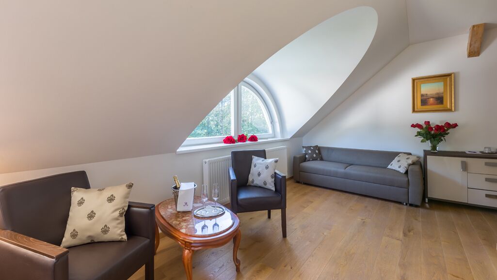 Un salón estilo loft con techo inclinado, un sofá gris, una mesa de centro de madera y vistas a través de un ventanal.