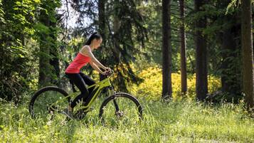 A person riding a mountain bike in a forested area with tall trees and green grass.