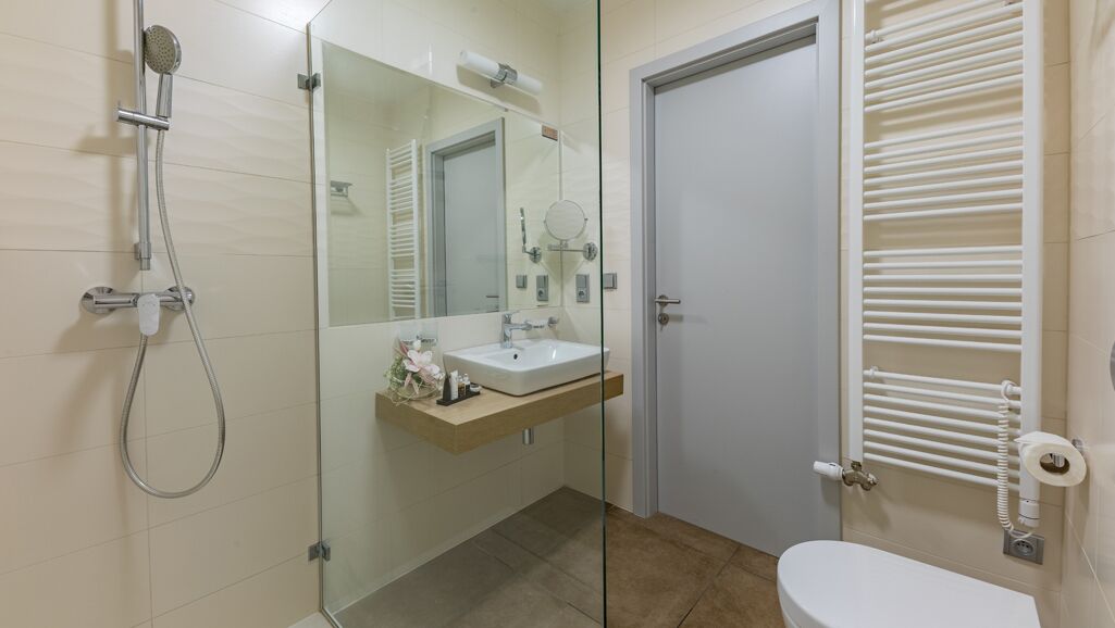 Un baño moderno con ducha de vidrio, un lavamanos blanco con espejo y un inodoro con perchero para toallas.