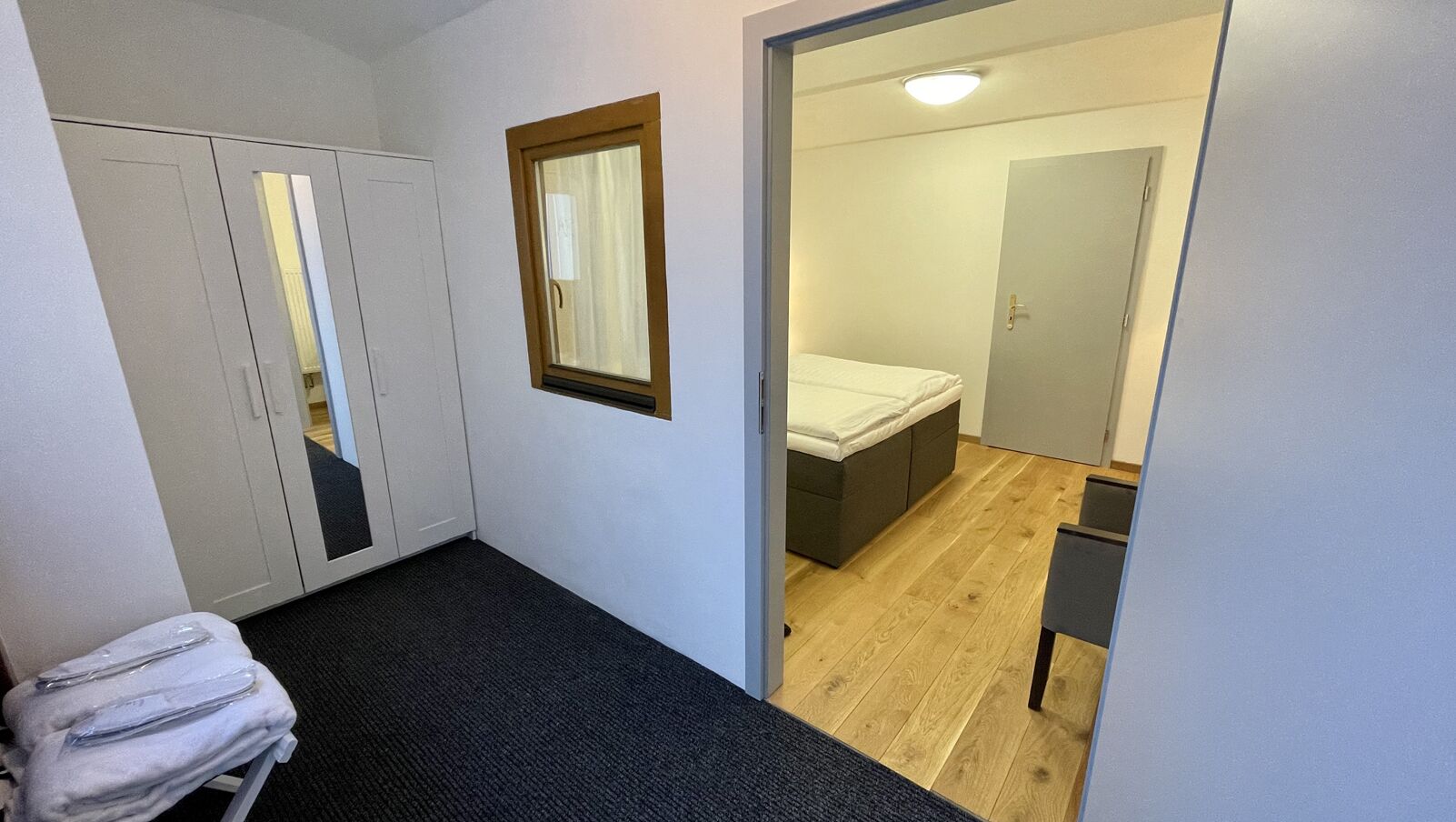 A compact bedroom with a bed, a wardrobe, and a small seating area.