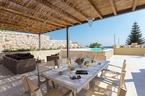 Un patio al aire libre con una mesa preparada para dos personas, un sofá de mimbre y un muro de piedra de fondo.