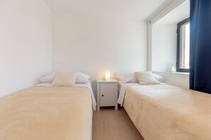 Habitación doble con dos camas, una mesita de noche con lámpara, ventana con cortinas y vistas al exterior.