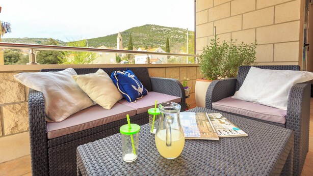 Un balcon avec des meubles en osier, une carafe en verre contenant une boisson et un magazine.