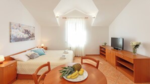 Une chambre d’hôtel avec un lit, une télévision, une table à manger avec des fruits et un tableau au mur.