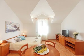 Une chambre d’hôtel avec un lit, une télévision, une table à manger avec des fruits et un tableau au mur.