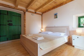 A bedroom with a wooden bed, a nightstand, a green door, and a small window. - Cypress Cottage - Four Bedroom House, Sleeps 8 (Dubrovnik)