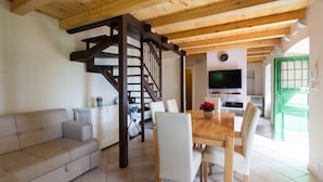Un salon moderne avec un plafond en bois, un canapé, une table à manger avec des chaises, un escalier et un coin cuisine équipé d’une télévision et doté d’une porte verte.