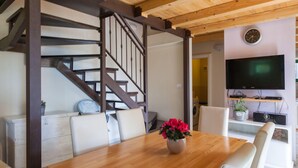 Un coin repas avec une table en bois, des chaises blanches, une plante en pot et un escalier avec des rampes en bois.