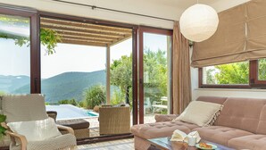 Une pièce avec vue sur les montagnes, comprenant un canapé, un fauteuil, une table et un luminaire suspendu.