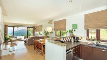 A modern kitchen with a dining area, large windows, and a view of the outdoors.