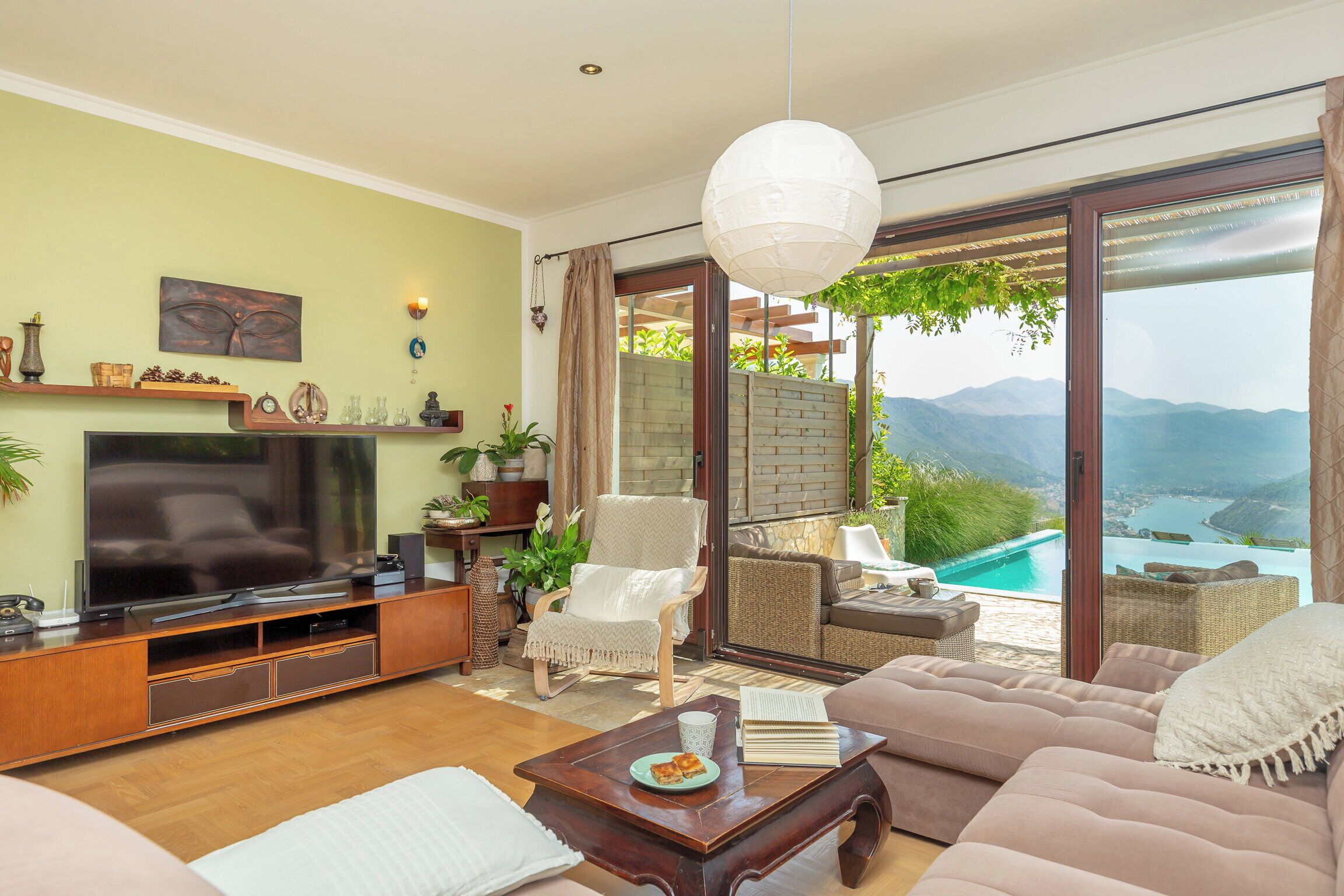 A living room with a TV, sofa, coffee table, and a view of mountains through large glass doors.