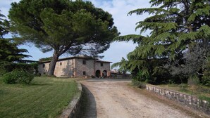 Edificio de piedra con camino de grava, rodeado de árboles y un área verde.