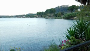 Ein ruhiger See mit Booten, umgeben von viel Grün und Gebäuden in der Ferne.