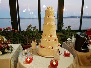 A multi-tiered wedding cake with roses on a table with candles, near a window with a view of the water. - Alb. Rist. Alfredo Da Persichella (Bracciano)