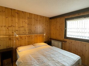 A bedroom with a wooden paneled wall, a bed with white bedding, a bedside table, and a window with a curtain. - Spacious apartment for 6 in Montgenèvre with parking (Montgenèvre)