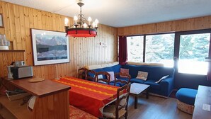 Een gezellig chaletinterieur met een eethoek, een bank en een raam met uitzicht op bomen.