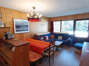 L’intérieur d’un chalet accueillant, avec un coin repas, un canapé et une fenêtre donnant sur les arbres.