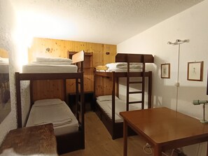 Een slaapzaal met stapelbedden, een houten tafel en een wandlamp.