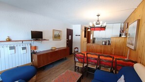 Een woonkamer met een zithoek, een televisie, een open haard en een keuken die zichtbaar is door een open deur.