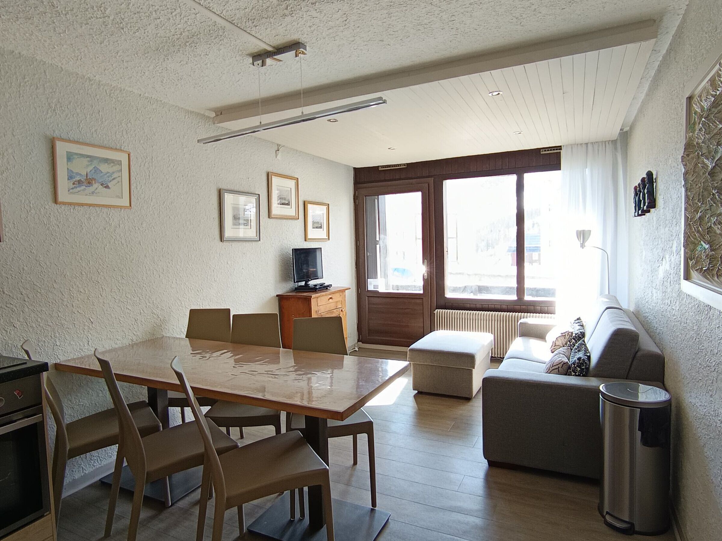 A modern living room with a dining area, a sofa, a TV, and a radiator.
