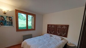 A bedroom with a large bed, a wooden floor, a window with a view of greenery, and a wall with decorative panels. - Comfortable apartment in Montgenèvre with balcony and parking (Montgenèvre)