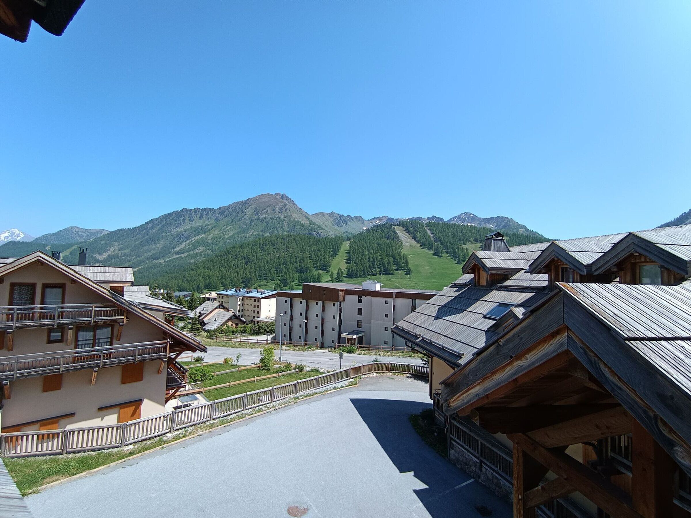 A mountain village with traditional wooden buildings, a clear sky, and a view of a mountain range.