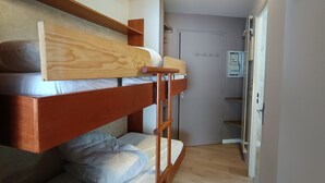 Ein Schlafraum mit Etagenbetten, einem Holz-Kopfteil, einer kleinen Ablage und einer Tür zu einem Badezimmer.