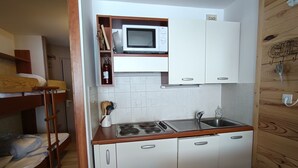 Eine kleine Küche mit Mikrowelle, Spüle und Schränken. Links befindet sich ein Etagenbett.