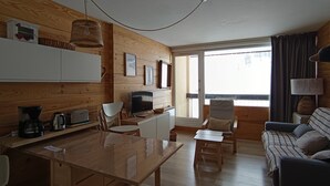 Ein gemütliches Blockhausszimmer mit Holzvertäfelung, einem Esstisch, einer Couch und einem Fernseher.