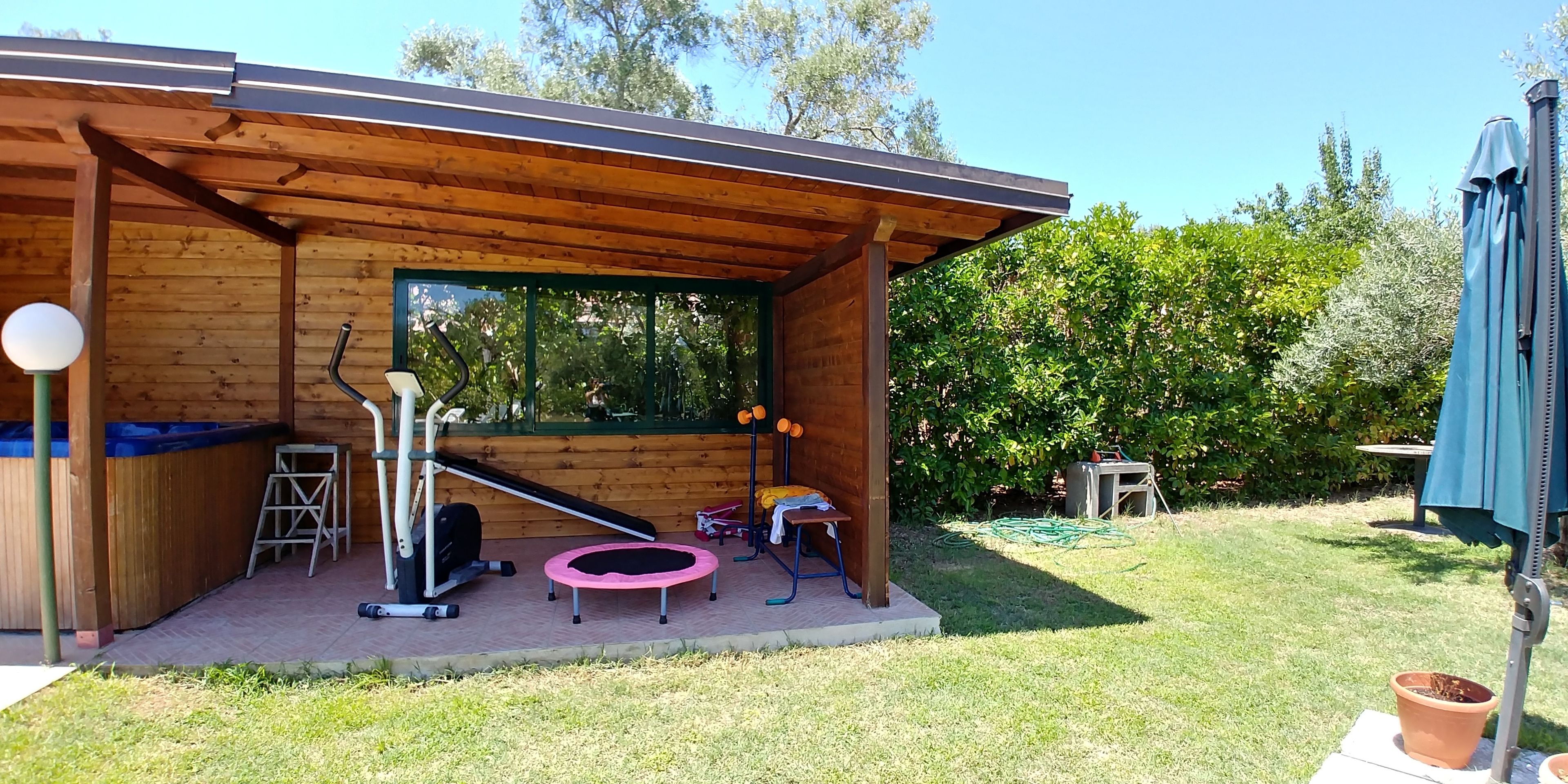 Une structure en bois dotée d’un patio couvert, d’équipements d’exercice et d’un trampoline.