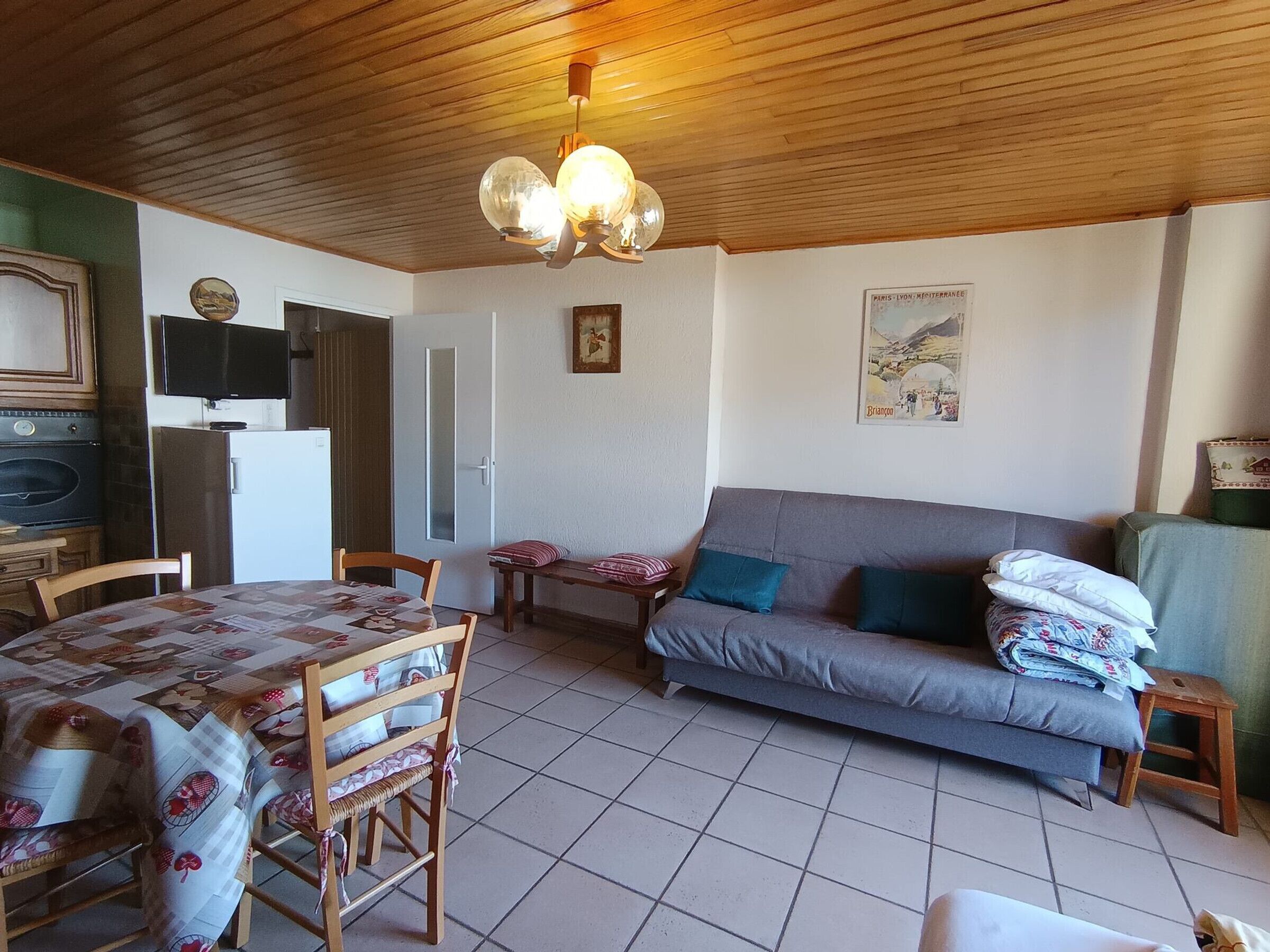 A cozy room with a wooden ceiling, a dining table with chairs, a sofa, and a television.