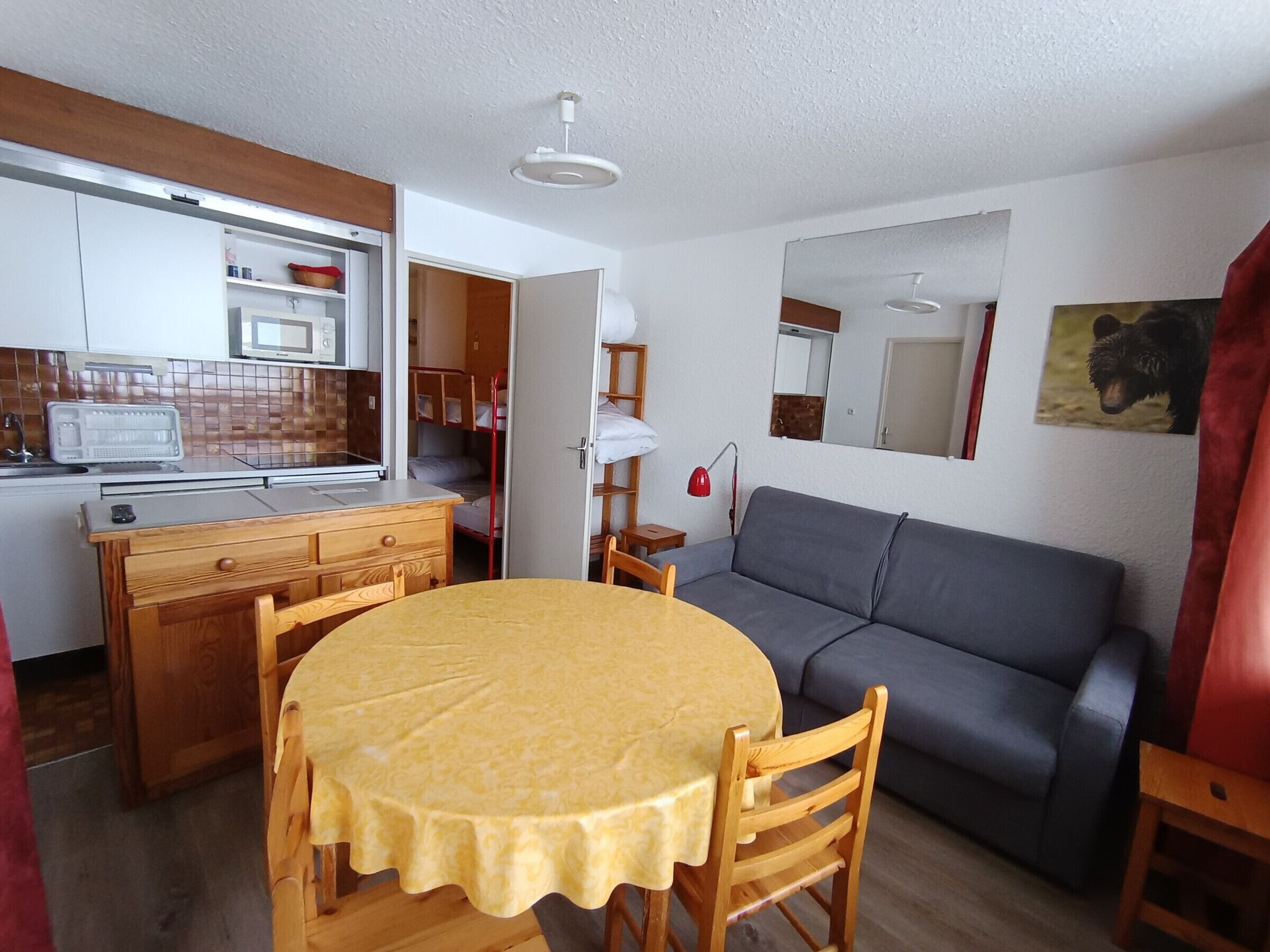 Een ruimtelijk ingerichte leefruimte met een kitchenette, een eethoek met tafel en stoelen, een bank en een rode stoel.
