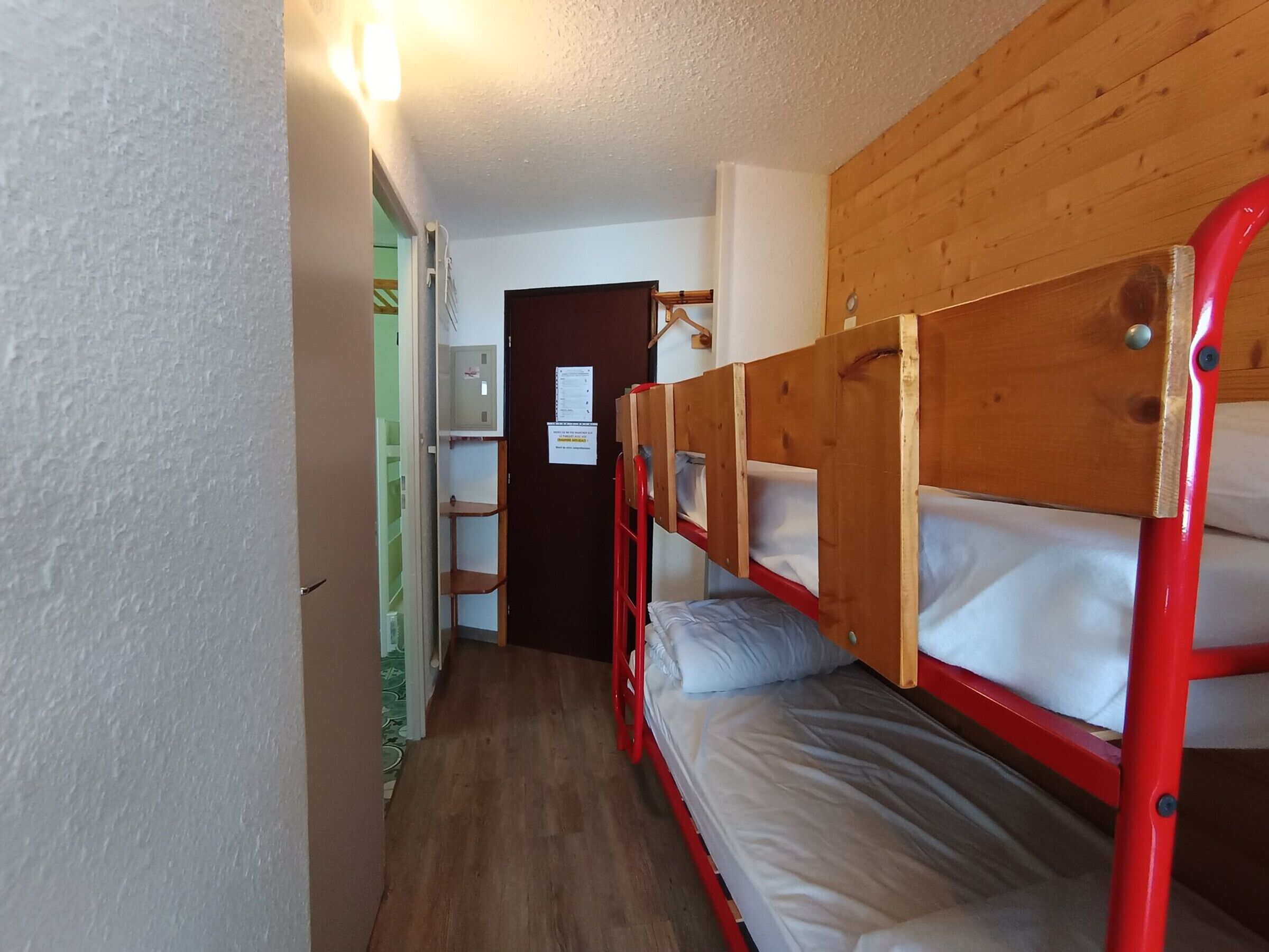 En smal hall med våningssängar på ena sidan och en dörr som leder till ett rum med en grön vägg och en vit dörr.