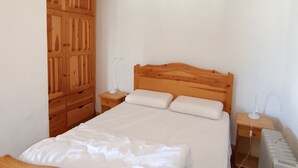 Une chambre avec une armoire en bois, un lit avec une literie blanche et une table de chevet avec une lampe.