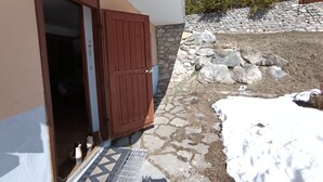 Un bâtiment avec une porte marron, un mur en pierre et un sol recouvert de neige.
