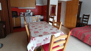 A compact room with a dining table, chairs, a bed, a kitchenette, and a bathroom.