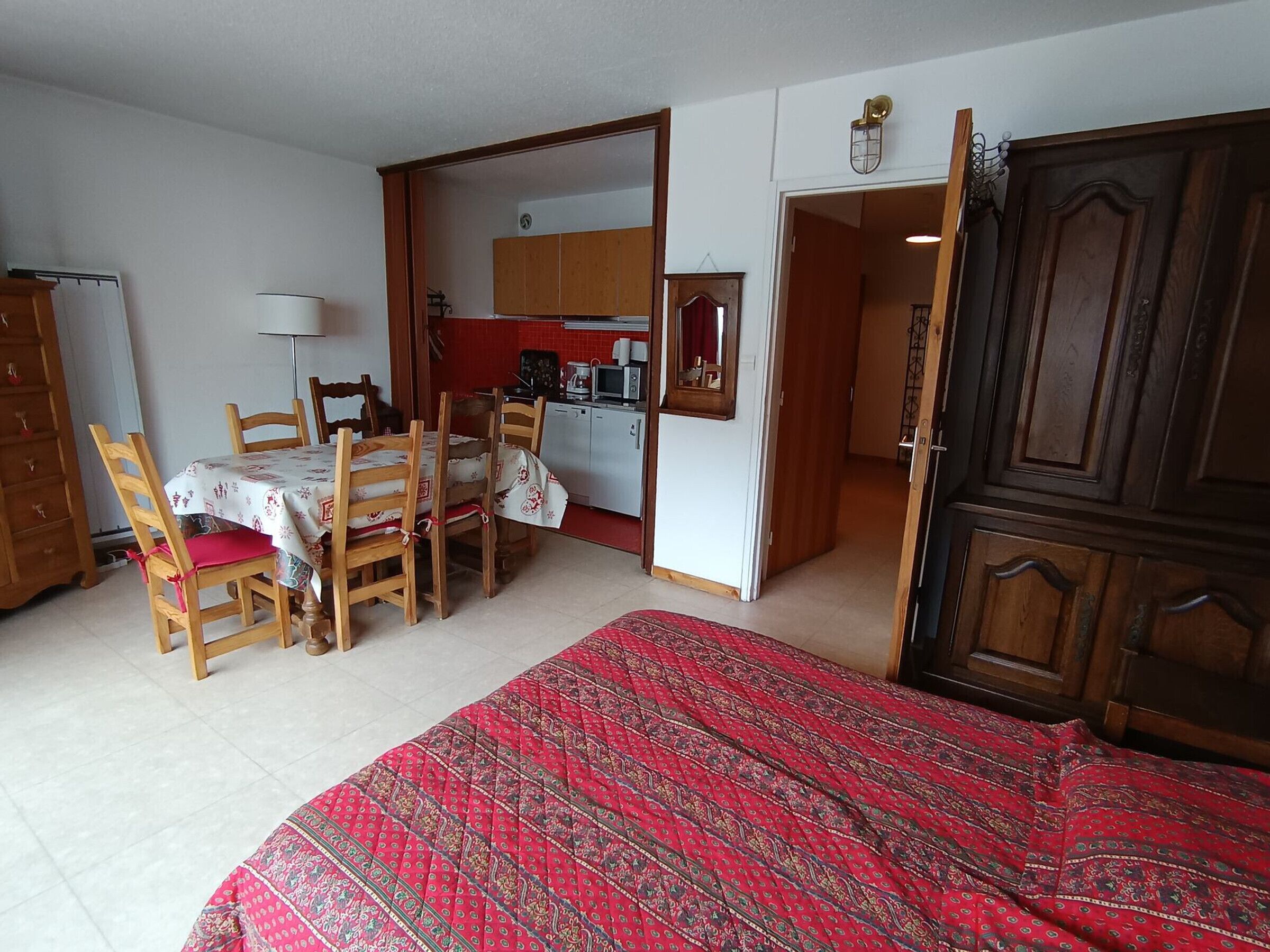 A compact room with a bed, a dining table with chairs, a kitchenette, and a wardrobe.